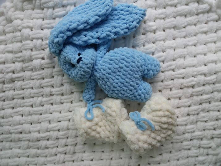 Зайчик плюшевий блакитного кольору на білому плюшевому дитячому пледі та дитячі плюшеві пінетки молочного кольору